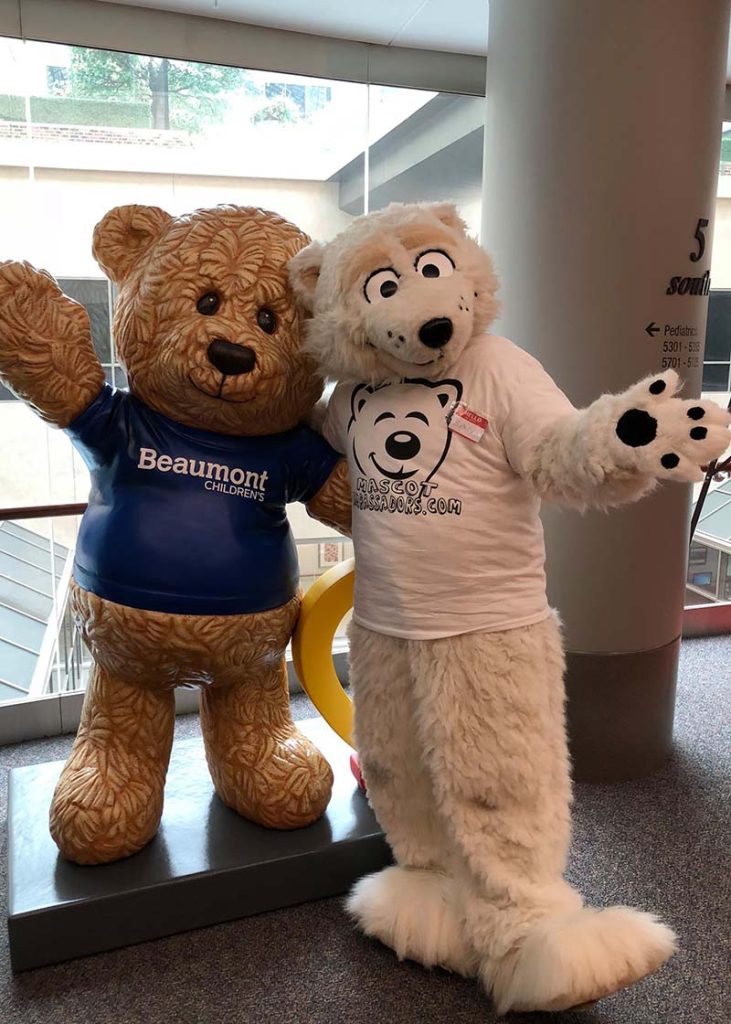 Hollywood Bear poses outdoors with two attendees at a community event.