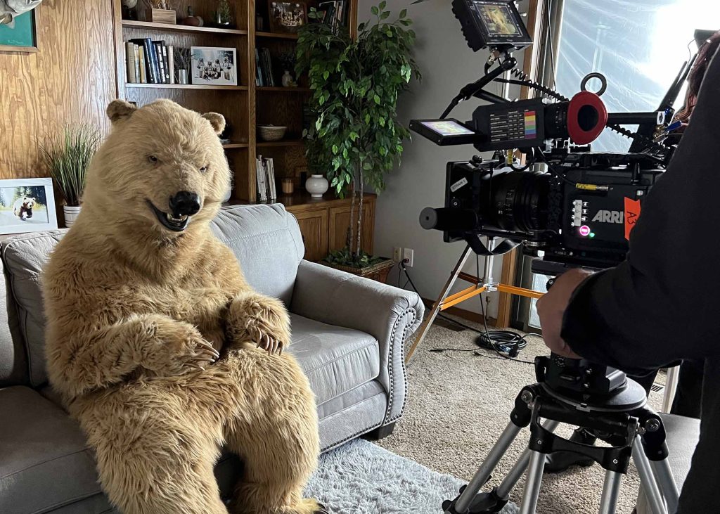 Hollywood Bear sits on a sofa in a living-room set while an ARRI cinema camera films the scene.