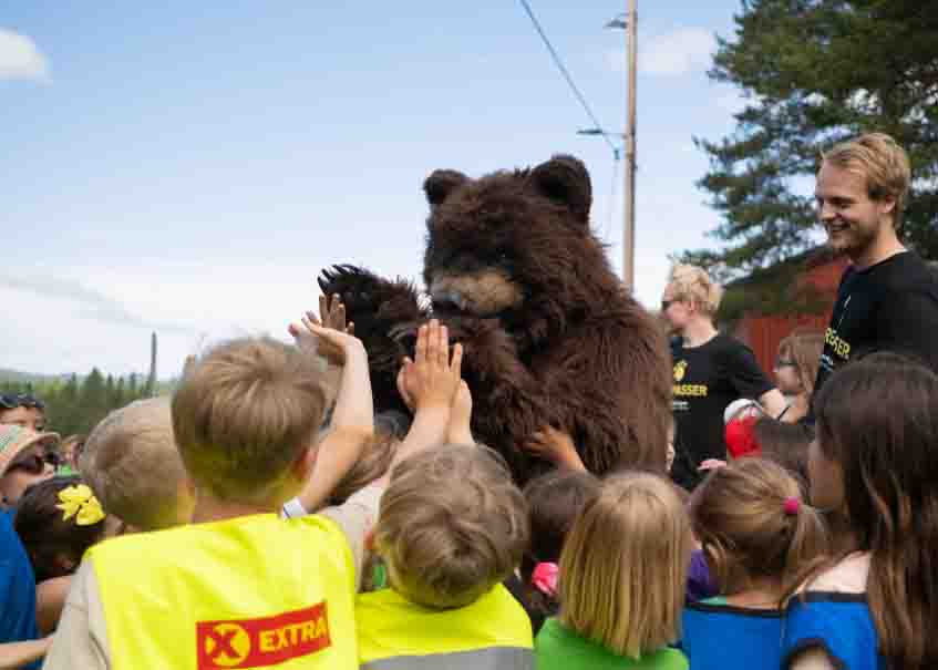 Hollywood Bear raises a paw to greet children at an outdoor community event in Trondheim.